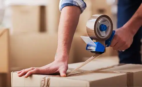 Hand sealing a cardboard box with packing tape.